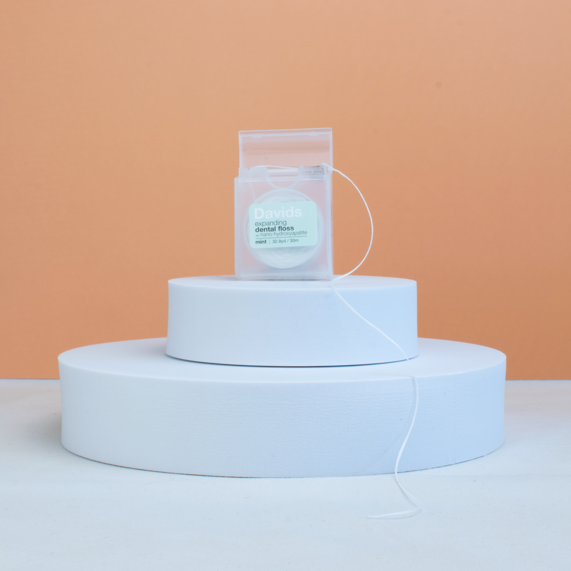 Davids bExpanding Dental Floss on a white platform with a peach background